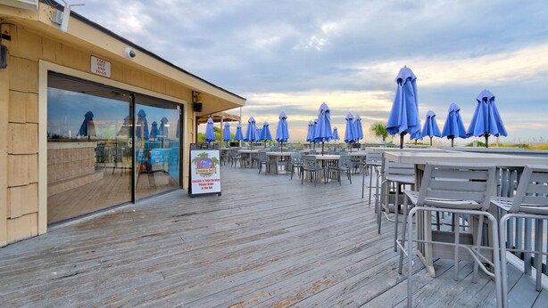 An outdoor seating area with tables and blue umbrellas, a wooden deck, and a sign for Jamaica's Jewel.