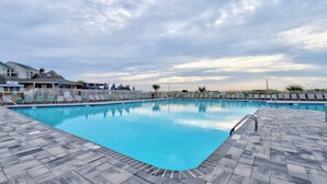 A rectangular swimming pool with a tiled deck, surrounded by lounge chairs and umbrellas, under a cloudy sky.