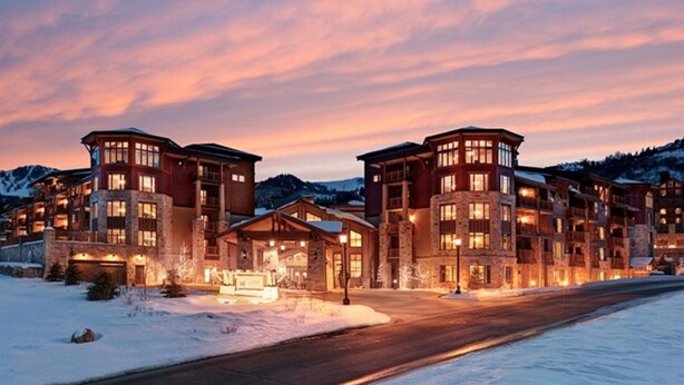 A multi-story hotel with a stone facade, large windows, and a snow-covered landscape at dusk.