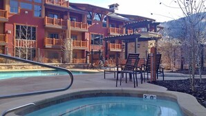 A pool area with lounge chairs, a wooden deck, and a building with balconies in the background.