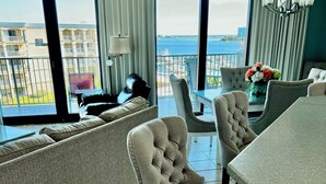 A modern living room with a sofa, two upholstered chairs, a dining table, and a view of the sea through large windows. - Free boat slip w/ Luxury 2 BR /Water front, on Terry Cove Condo  (Orange Beach)