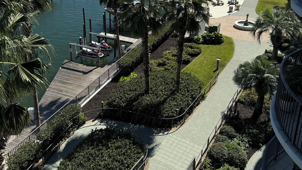 A marina with boats docked, a pathway lined with palm trees, and a view of the water and distant buildings. - Free boat slip w/ Luxury 2 BR /Water front, on Terry Cove Condo  (Orange Beach)