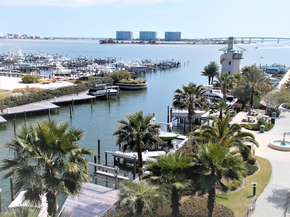 A marina with boats docked, a lighthouse, and a bridge in the background.