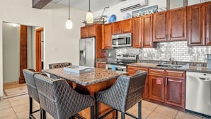 A kitchen with wooden cabinets, granite countertops, a stainless steel refrigerator, a microwave, a stove, and a dishwasher. - Shadow Palm Villa 2 Private Resort Villa (Port Aransas)