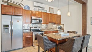 A kitchen with wooden cabinets, stainless steel appliances, a granite countertop, and a dining area with leather chairs. - Shadow Palm Villa 2 Private Resort Villa (Port Aransas)