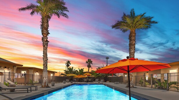 A swimming pool with palm trees and umbrellas, surrounded by lounge chairs and a fence. - Shadow Palm Villa 2 Private Resort Villa (Port Aransas)