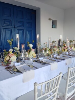 Una larga mesa de comedor vestida con manteles blancos, velas y arreglos florales.