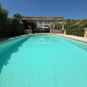 Ein klares Schwimmbecken mit einer Steinmauer und einem Pergola im Hintergrund.