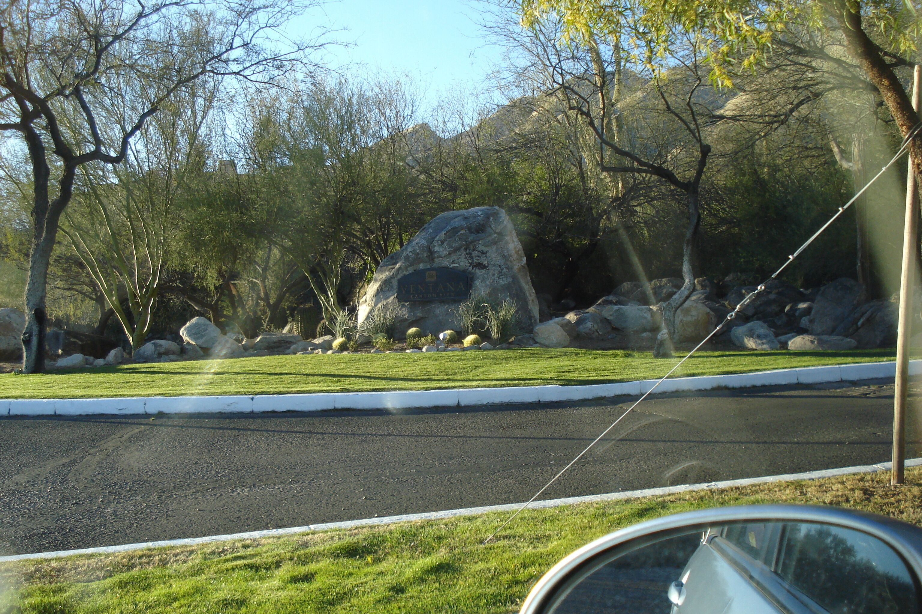 Una carretera con una gran roca en el centro, rodeada de árboles y un área verde.