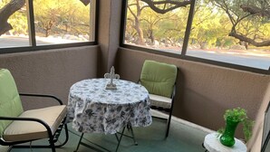 En liten uteplats med ett runt bord täckt av en blommig duk, två stolar och ett litet sidobord med en grön växt.