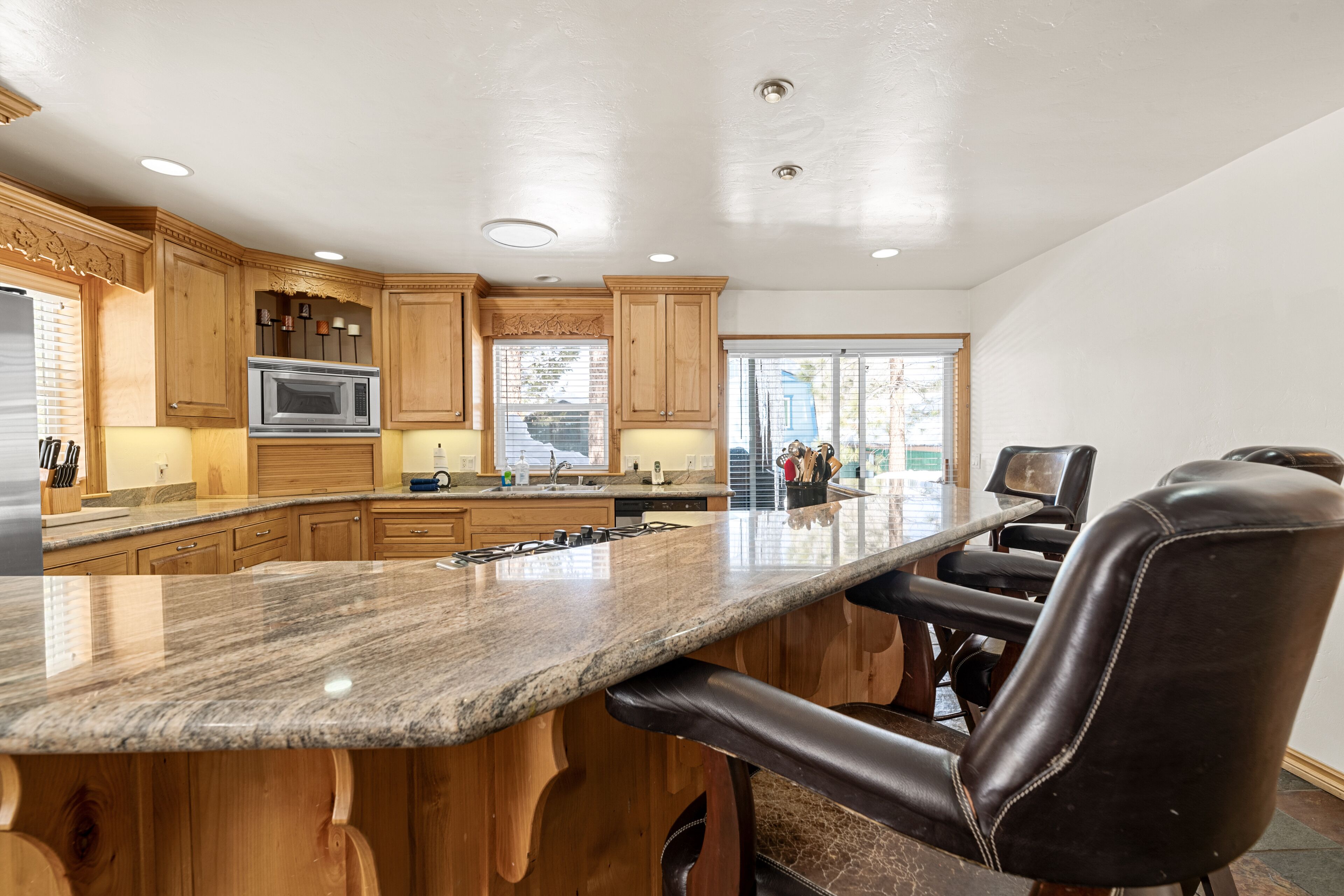 A kitchen with wooden cabinets, a granite countertop, a built-in microwave, and a bar area with leather barstools.