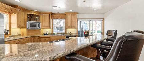 A kitchen with wooden cabinets, a granite countertop, a built-in microwave, and a bar area with leather barstools.