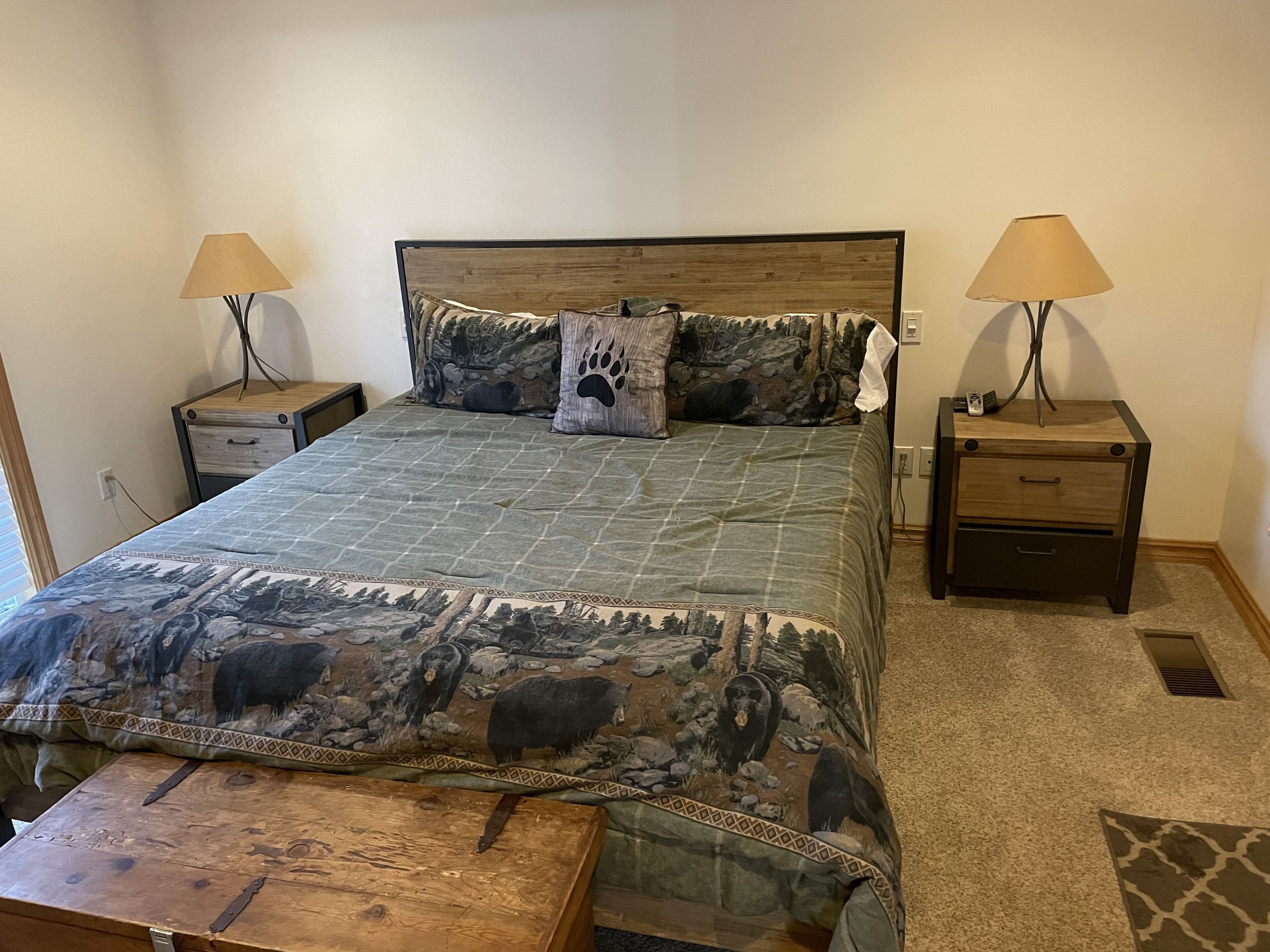 A bedroom with a bed, two nightstands, two lamps, a wooden bench, and a carpeted floor.