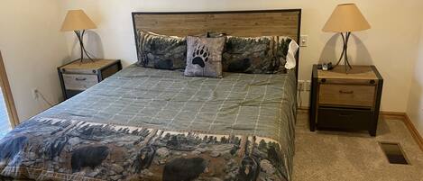 A bedroom with a bed, two nightstands, two lamps, a wooden bench, and a carpeted floor.
