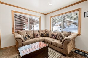 A living room with a sectional sofa, a coffee table, and two windows with blinds. - Bear mountain resort 5bd 3 bath sleeps 2600 sq (Big Bear Lake)