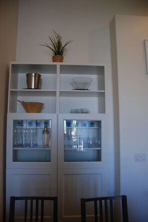 A white cabinet with shelves containing various kitchenware and a potted plant.