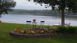 A lakeside seating area with a table and two chairs, surrounded by a flower bed. - Authentic Alaskan slice of heaven (Wasilla)