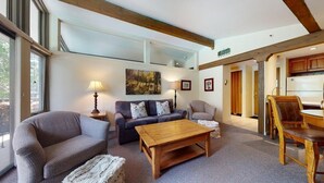 A spacious living room with a large window, a sofa set, a wooden coffee table, and a dining area with a chair and table.