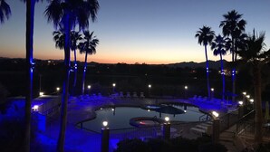 A pool area with lounge chairs and palm trees, surrounded by a fence and illuminated by blue lights.