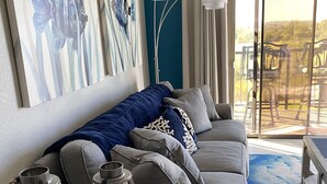 A modern living room with a grey sofa, blue and white cushions, a wooden coffee table with lanterns, and abstract wall art.