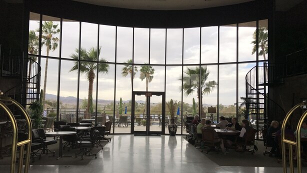 A spacious indoor area with large windows offering views of palm trees and mountains.