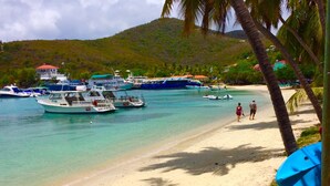 A beach with boats docked, a sandy shore, and palm trees. - Grande Bay SURFSIDE Studio, Beachfront, Perfect View/Location (Cruz Bay)