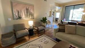 Un salon comprenant un canapé, deux fauteuils, une table basse, un tapis, une lampe et un tableau représentant un cactus accroché au mur.