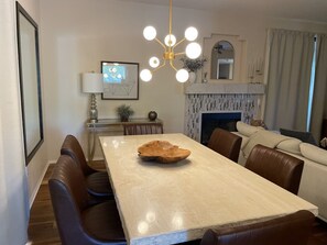 Un comedor moderno con una mesa grande, sillas de cuero, un original cuenco de madera como centro de mesa, una araña y una chimenea.