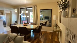 Un espace de repas moderne avec une grande table, des chaises et un lustre. On y trouve également un canapé et une petite table avec une lampe et des objets décoratifs.