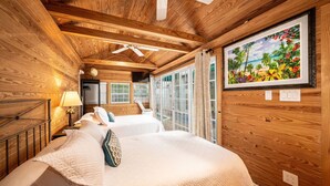 Un dormitorio de cabaña de madera con dos camas, un ventilador de techo y un ventanal con cortinas.