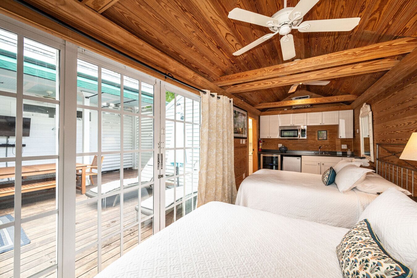 A cabin with two beds, a kitchenette, and a deck with outdoor seating.