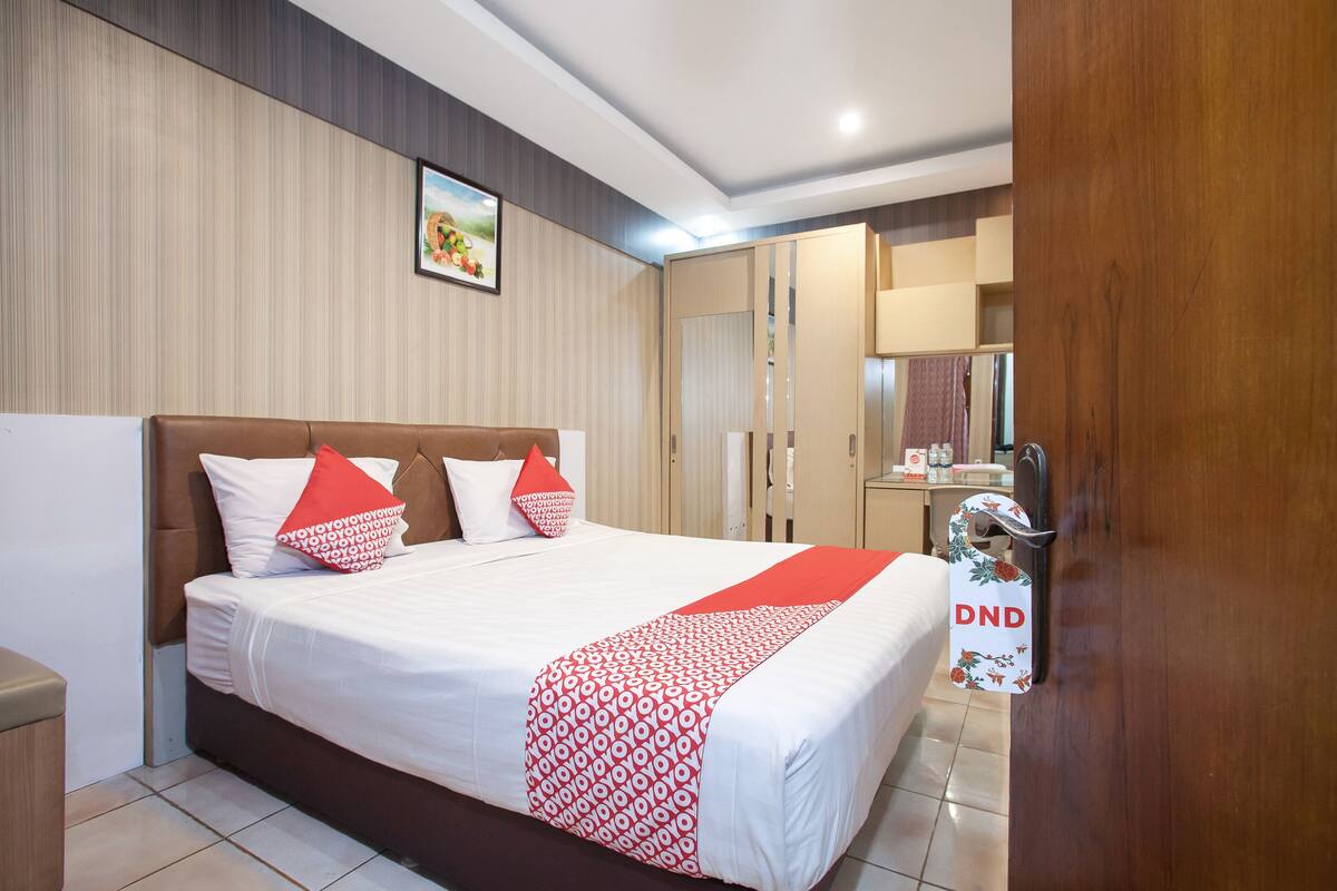 A modern hotel room with a large bed, wooden wardrobe, and a bathroom visible through an open door.