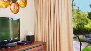 Ein Zimmer mit Fernseher auf einem Holztisch, einer Taschentuchbox und einem Fenster mit Vorhängen.
