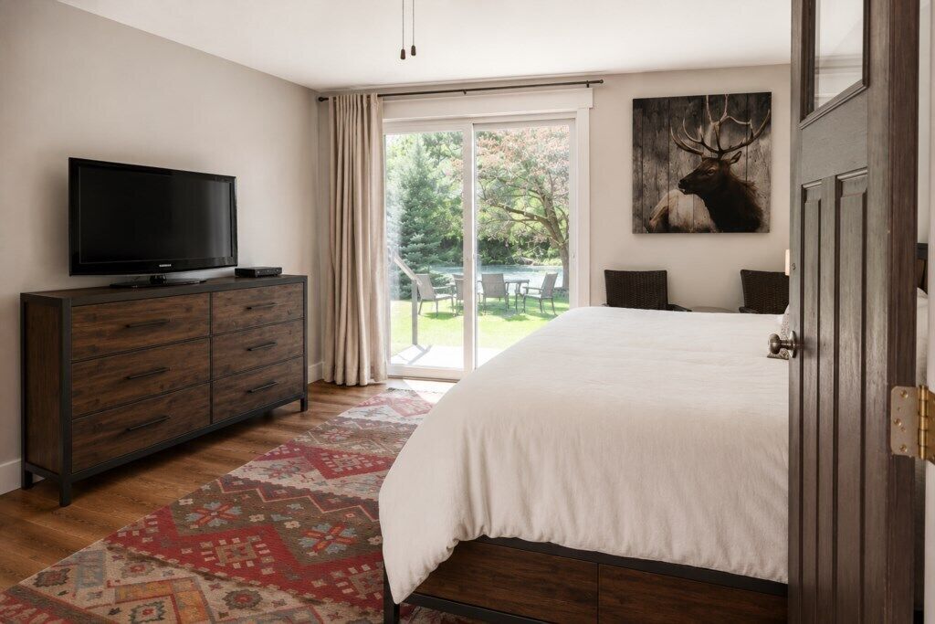 Une chambre avec un grand lit, un téléviseur posé sur une commode en bois et une porte-fenêtre coulissante donnant sur un espace extérieur.