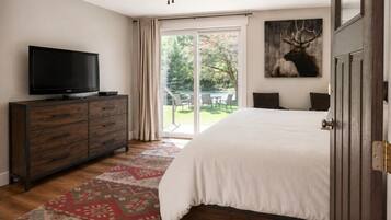 Une chambre avec un grand lit, un téléviseur posé sur une commode en bois et une porte-fenêtre coulissante donnant sur un espace extérieur.