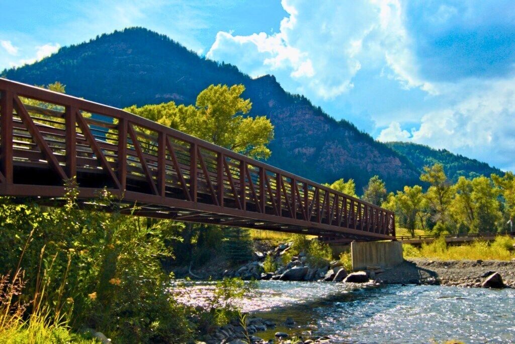 A metal bridge over a river with mountains in the background.
