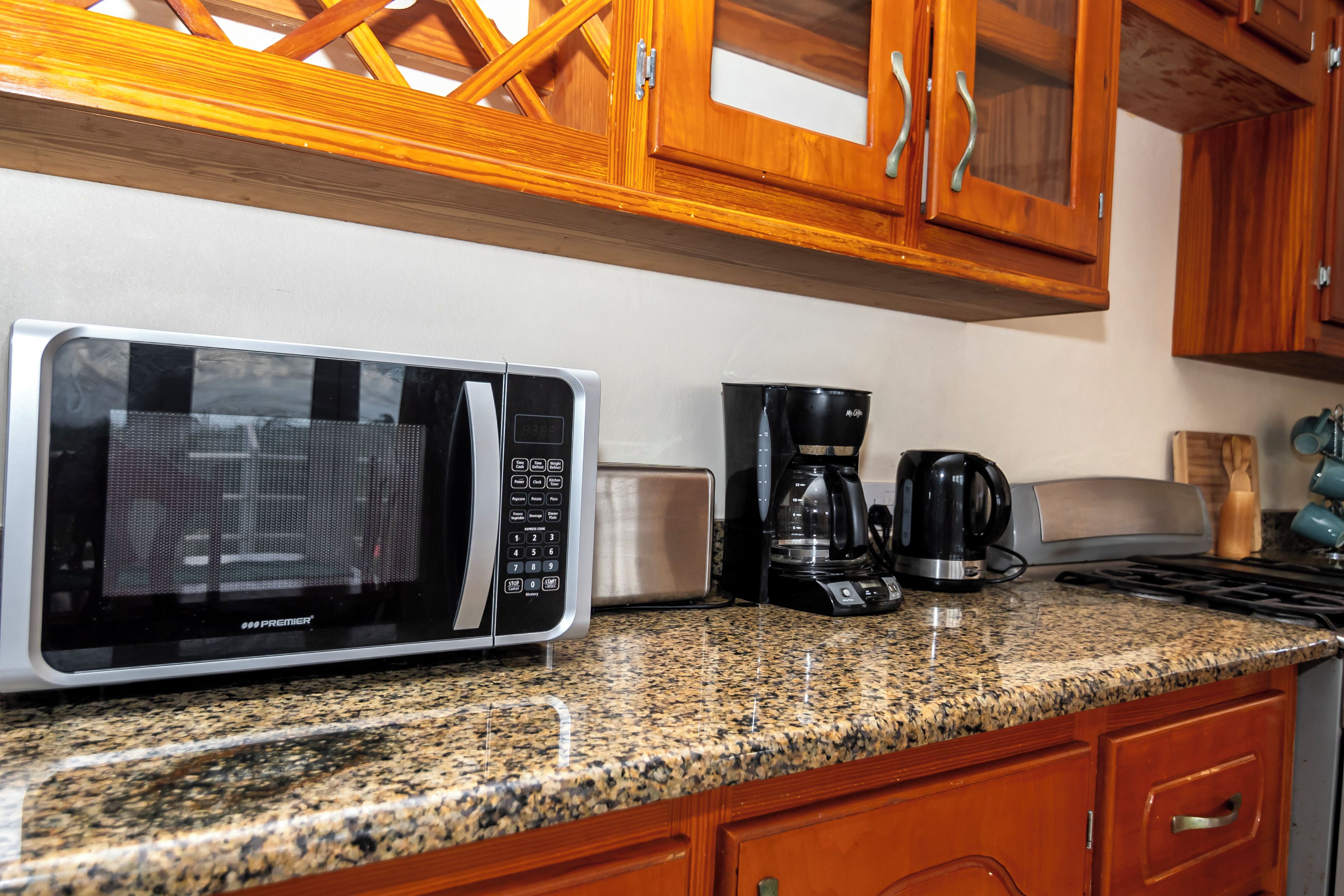 Una cocina con microondas, cafetera, tostadora y armarios de madera.