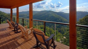 A wooden deck with rocking chairs overlooking a mountainous landscape.