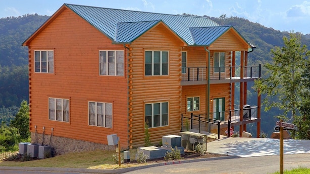 A two-story log cabin with a metal roof, a balcony, and a view of the mountains.