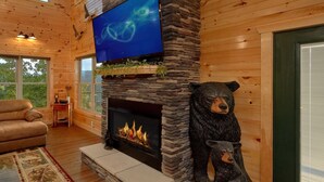 A cozy living room with a stone fireplace, a bear sculpture, and a television mounted above it.