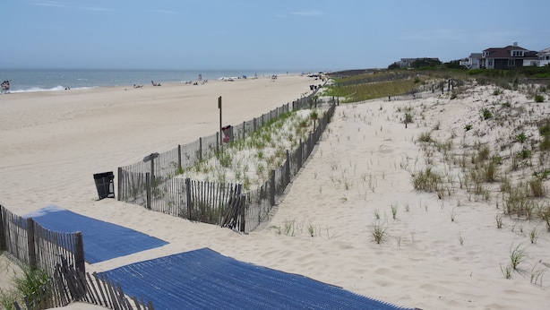 Een strand met een houten omheining en een blauwe mat die naar het water leidt.