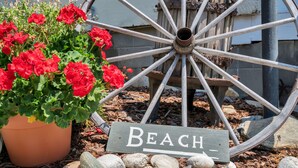 Une roue en bois sur laquelle est fixé un panneau indiquant « Plage », ainsi qu’une plante en pot ornée de fleurs rouges.