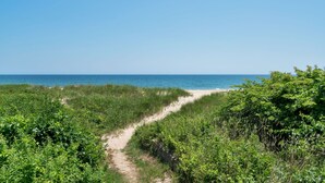 Un sentier côtier qui mène à une plage bordée de part et d’autre par une végétation luxuriante.