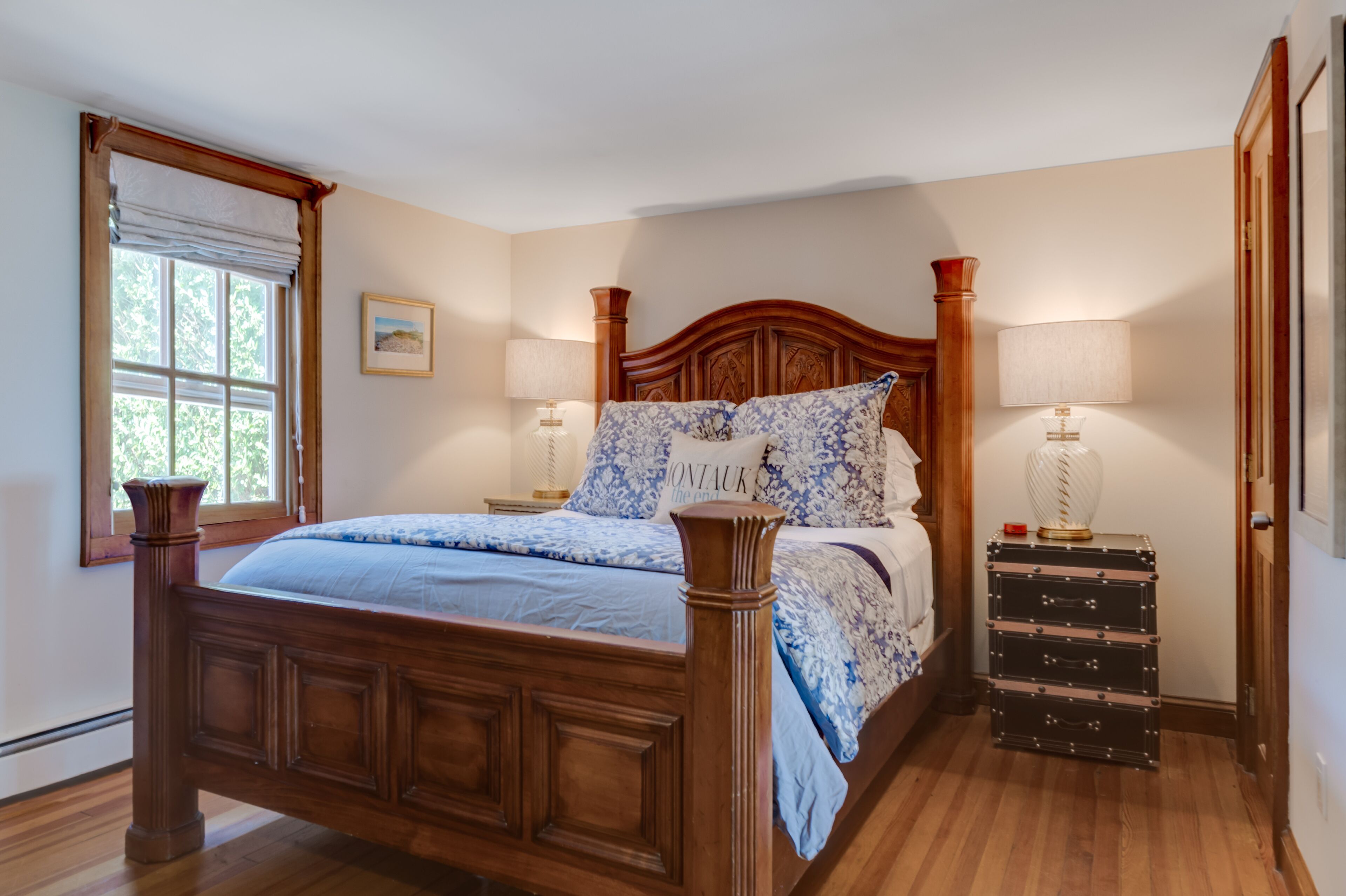 Un dormitorio con una cama de madera, dos lámparas de noche, una mesita de noche y una ventana con cortinas.