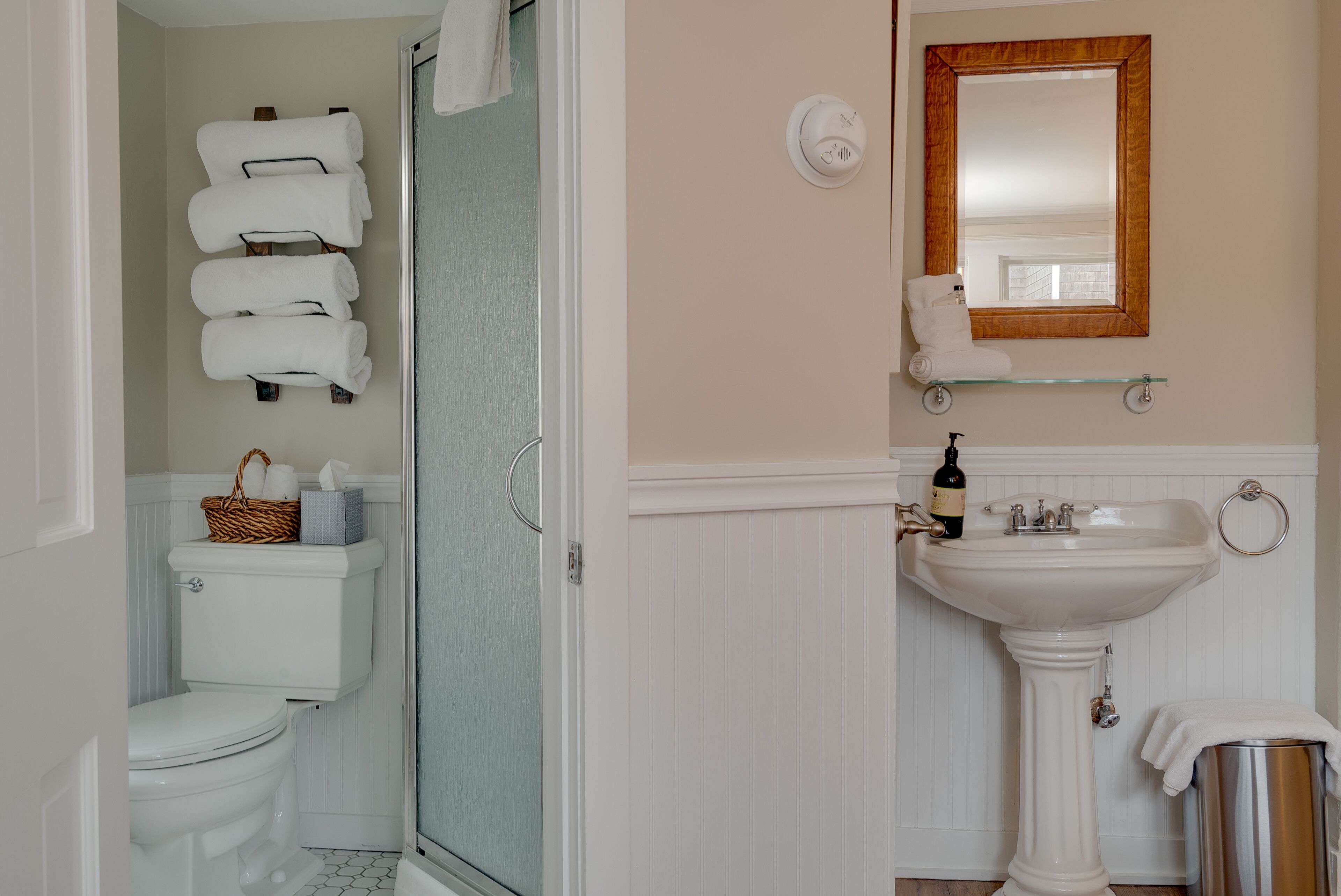 Ein Badezimmer mit Toilette, einer Duschkabine aus Glas, einem Waschbecken mit Spiegel und Handtüchern an einem Ablagefach.