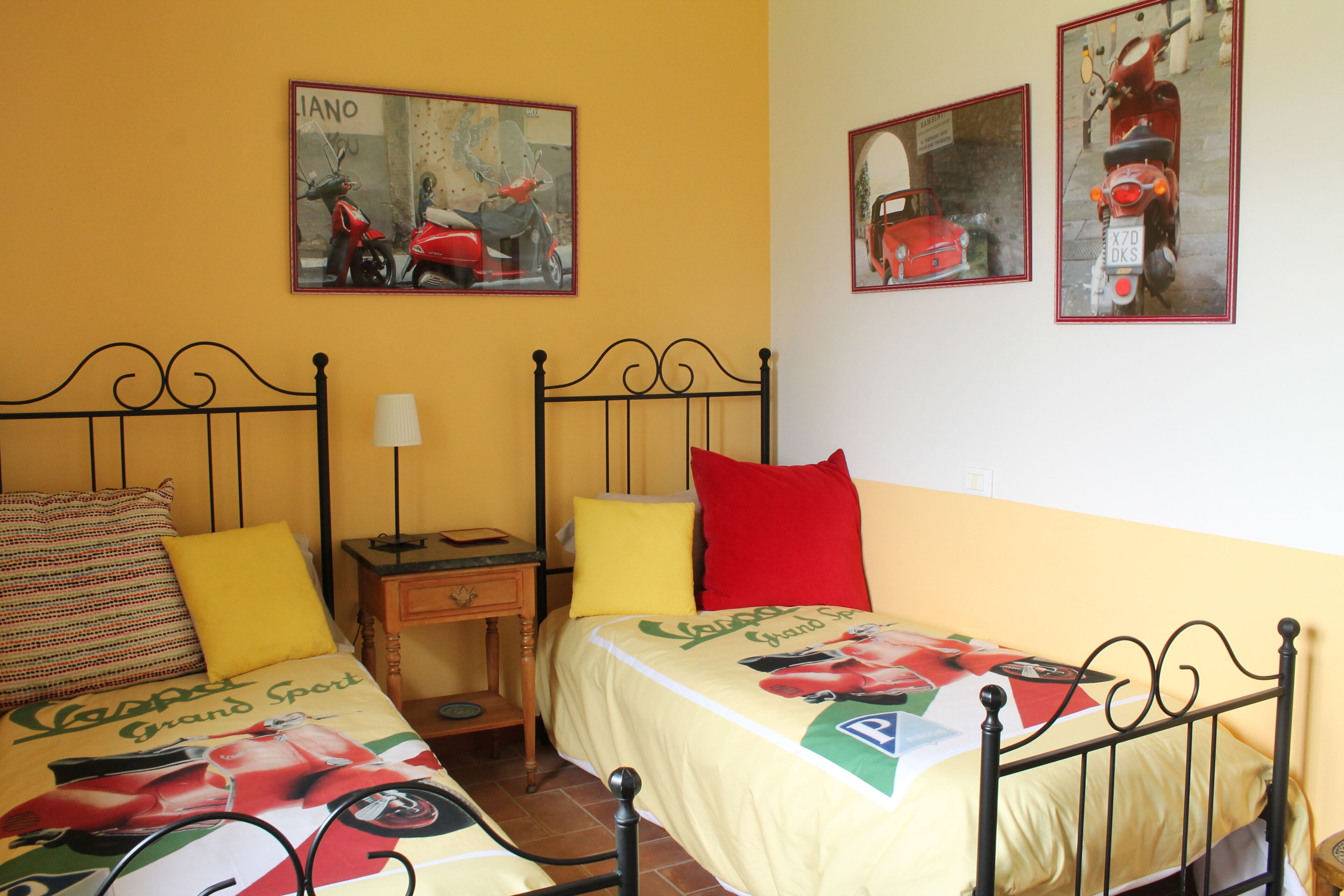 A room with two beds, each with a unique bedspread, a nightstand, a lamp, and two framed pictures on the wall.