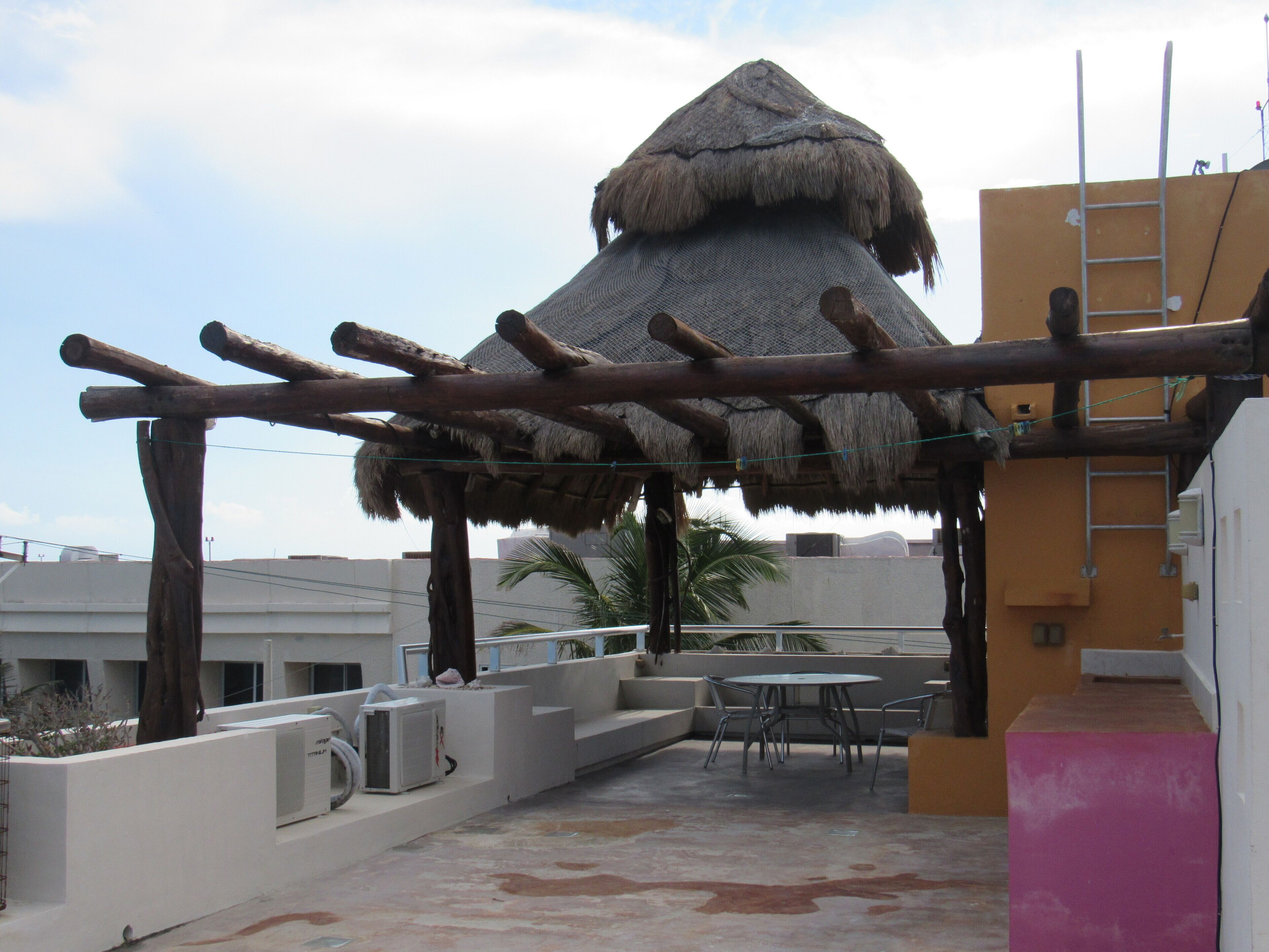 Une terrasse sur le toit, dotée d’une structure avec un toit de chaume, d’un espace salon extérieur et offrant une vue sur les bâtiments environnants.