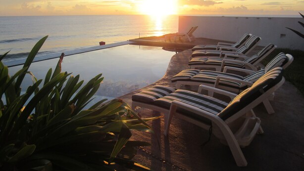 An infinity pool with lounge chairs facing the ocean at sunset. - Breathtaking 7 Bedroom Villa on the Ocean with a Infinity Private Pool (Isla Mujeres)