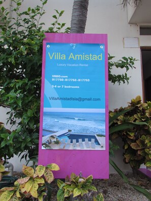 A sign for Villa Amistad, a luxury vacation rental with 3-4 or 7 bedrooms, contact information, and a view of the ocean.