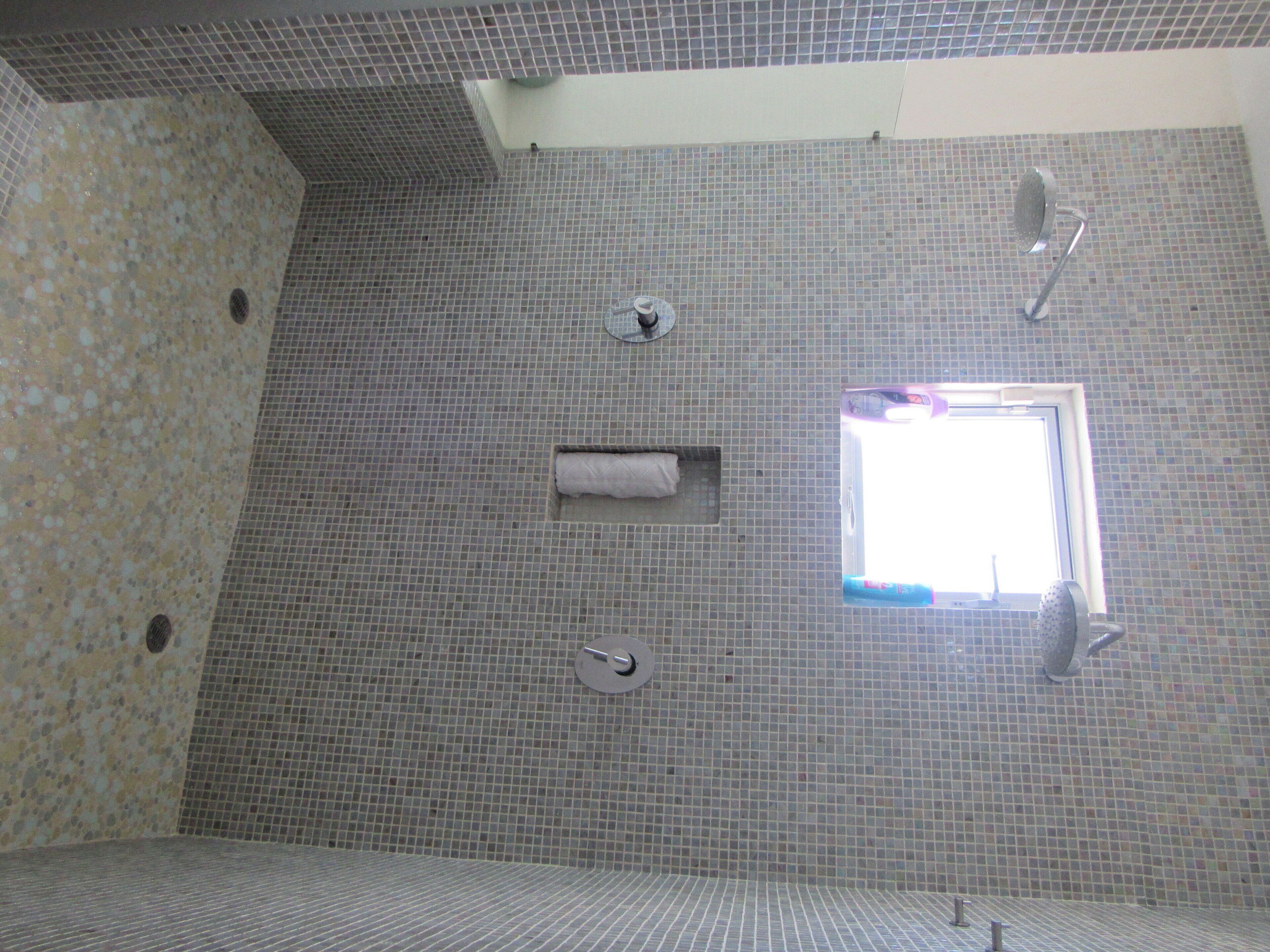 A bathroom with a tiled floor, a shower area, and a window.